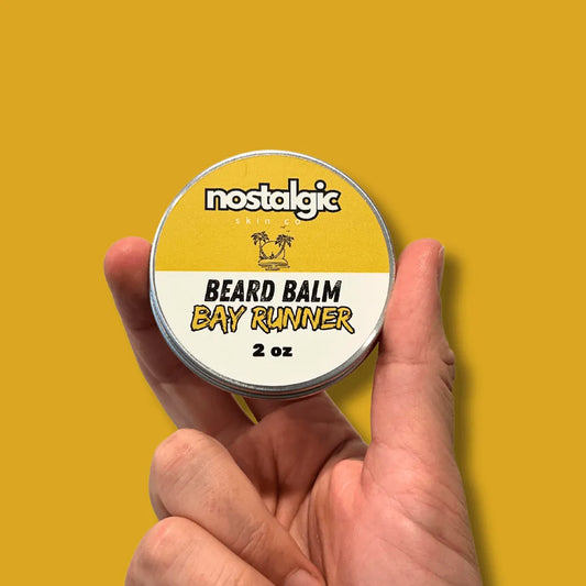 A tin of Bay Runner Beard Balm open to reveal a rich, conditioning balm, placed beside natural ingredients like shea butter and essential oils.