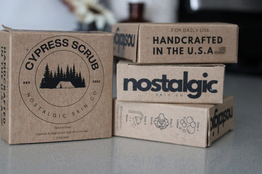 Stacked boxes of Nostalgic Skin Co. handmade bar soaps with eco-friendly packaging, showcasing rustic, natural branding on a clean countertop.”
