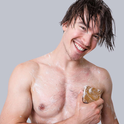 Smiling man with wet hair holding pine tar bar soap in a playful shower scene, showcasing the best men's soap.