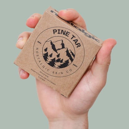 Hand holding Pine Tar Bar Soap by Nostalgic Skin Co., featuring eco-friendly packaging and mountain logo design.