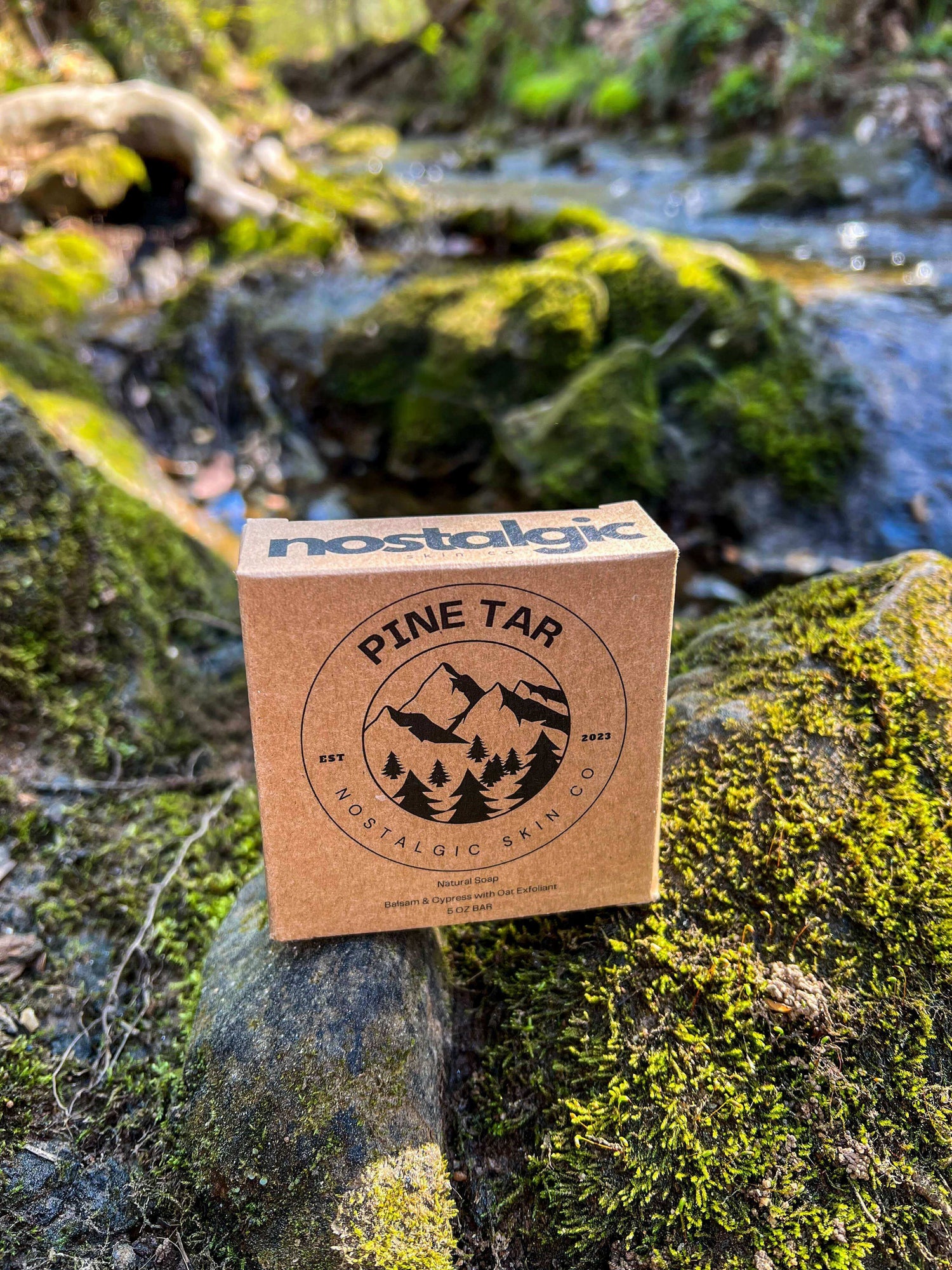 Packaged Pine Tar Soap bars stacked on vibrant green moss in a forest setting, emphasizing the natural and earthy essence of Nostalgic Skin Co. products